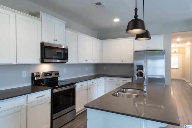 kitchen with appliances with stainless steel finishes, decorative light fixtures, a kitchen island with sink, and sink