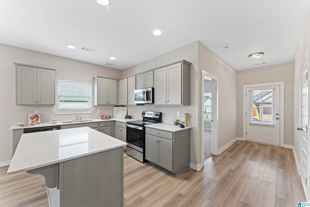 kitchen with gray cabinetry, sink, light hardwood / wood-style flooring, appliances with stainless steel finishes, and a kitchen island