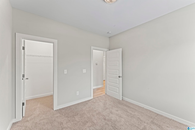 unfurnished bedroom featuring a walk in closet, a closet, and light colored carpet