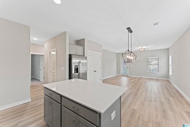 kitchen with pendant lighting, a center island, stainless steel refrigerator with ice dispenser, gray cabinets, and light wood-type flooring