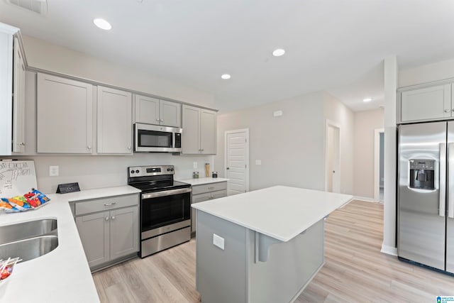 kitchen with sink, gray cabinets, light wood-type flooring, appliances with stainless steel finishes, and a kitchen island