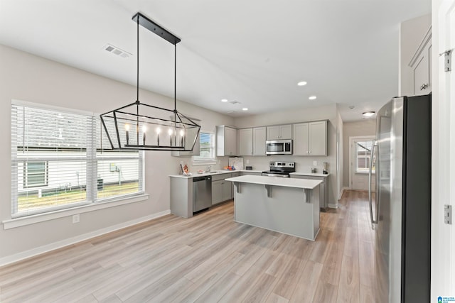 kitchen with a wealth of natural light, pendant lighting, stainless steel appliances, and light hardwood / wood-style floors