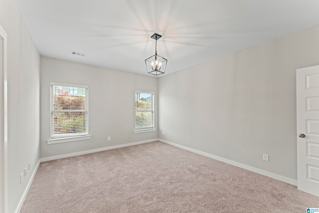 spare room featuring a wealth of natural light, light colored carpet, and an inviting chandelier