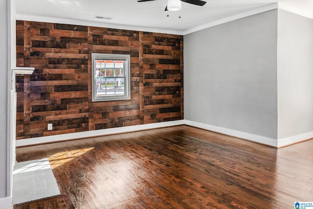 unfurnished room with wood-type flooring, ceiling fan, ornamental molding, and wood walls