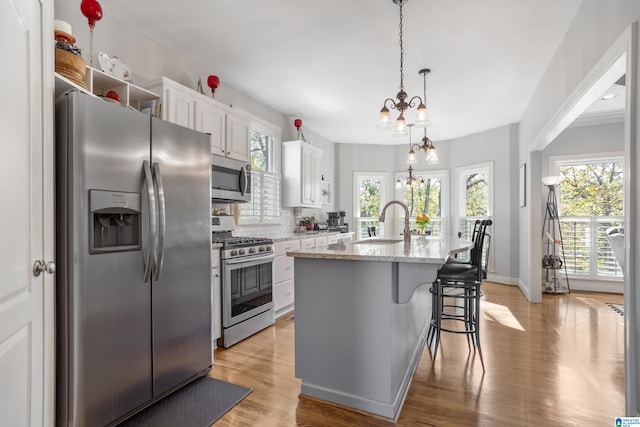 kitchen with decorative light fixtures, an island with sink, appliances with stainless steel finishes, a notable chandelier, and white cabinetry