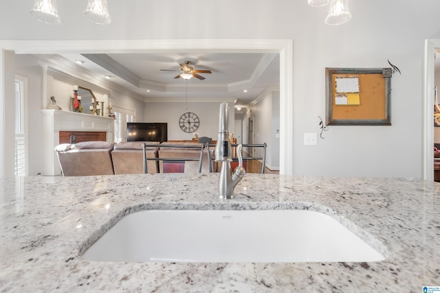 kitchen with light stone counters, a tray ceiling, crown molding, sink, and a fireplace