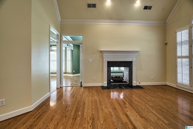 unfurnished living room featuring a high end fireplace, wood-type flooring, crown molding, and a healthy amount of sunlight