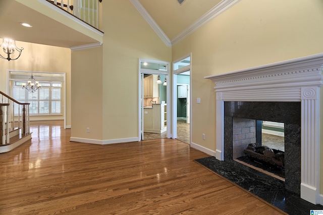 unfurnished living room featuring a premium fireplace, high vaulted ceiling, a notable chandelier, wood-type flooring, and ornamental molding