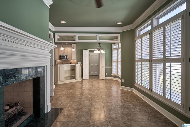 entryway with ceiling fan with notable chandelier, dark tile patterned floors, ornamental molding, and a fireplace