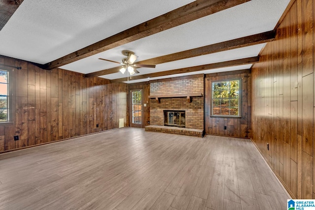 unfurnished living room with wooden walls, a fireplace, a textured ceiling, beamed ceiling, and light hardwood / wood-style floors