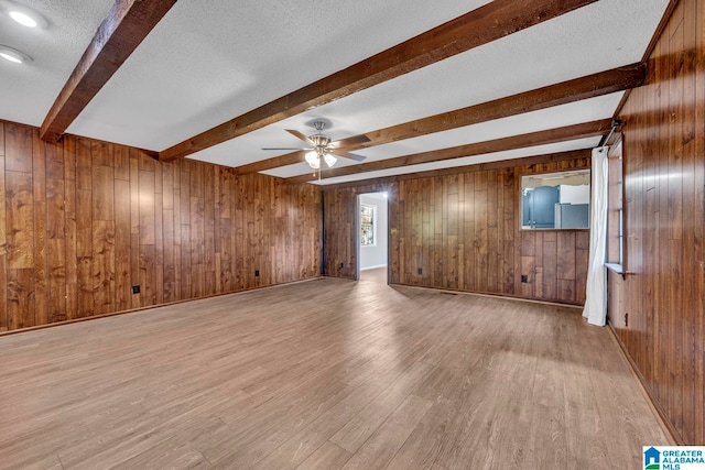 unfurnished living room with ceiling fan, beam ceiling, wooden walls, and light hardwood / wood-style flooring