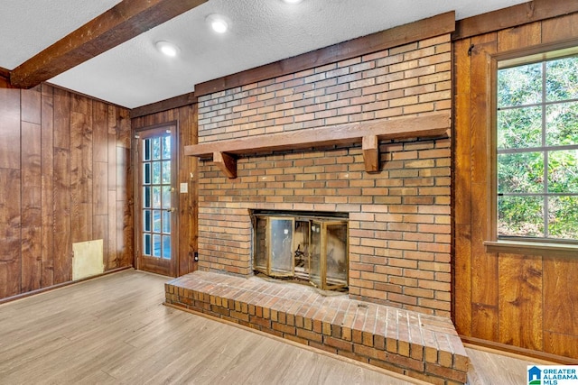 unfurnished living room with a fireplace, wood walls, light hardwood / wood-style flooring, and a textured ceiling