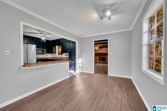 interior space featuring ornamental molding, kitchen peninsula, a textured ceiling, appliances with stainless steel finishes, and hardwood / wood-style flooring