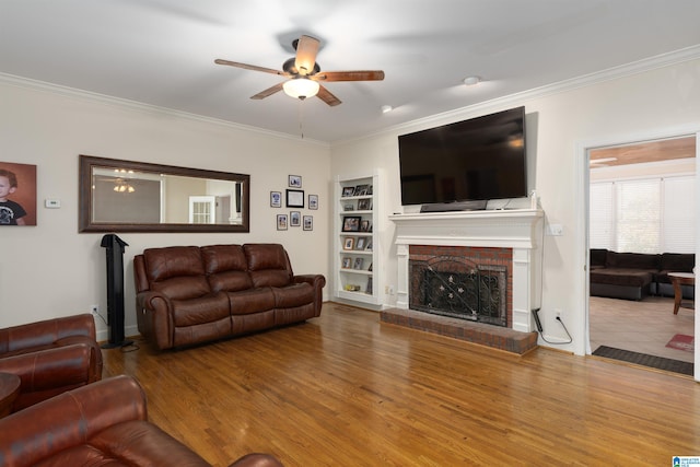 living room with hardwood / wood-style floors, crown molding, ceiling fan, built in features, and a fireplace