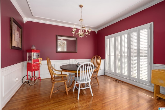 dining room with a wealth of natural light, an inviting chandelier, ornamental molding, and hardwood / wood-style flooring