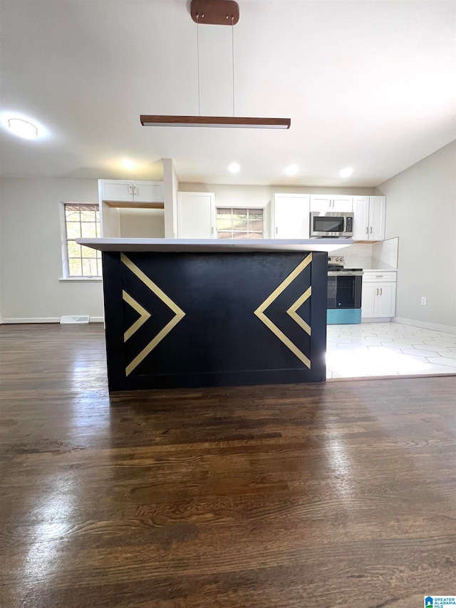 interior space featuring dark wood-type flooring, white cabinets, hanging light fixtures, and appliances with stainless steel finishes