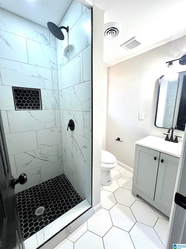 bathroom with a tile shower, tile patterned flooring, vanity, and toilet