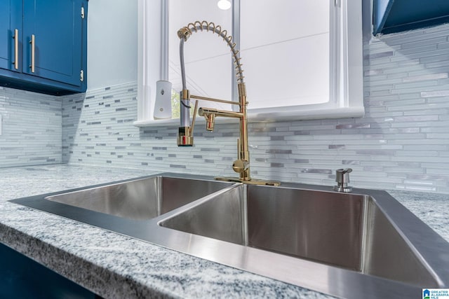 details featuring blue cabinets, sink, light stone countertops, tasteful backsplash, and white cabinetry