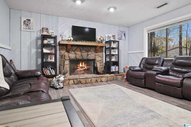 living room featuring hardwood / wood-style flooring, wood walls, a stone fireplace, and a textured ceiling