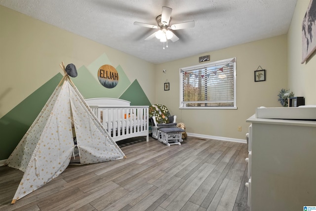 bedroom with ceiling fan, light wood-type flooring, a textured ceiling, and a nursery area