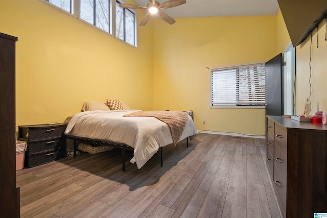 bedroom with a towering ceiling, light wood-type flooring, and ceiling fan