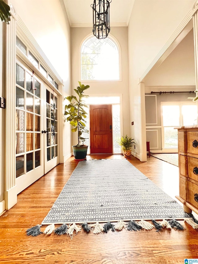 entryway with a high ceiling, light wood-type flooring, an inviting chandelier, and crown molding