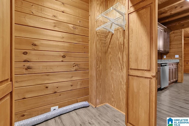 interior space with light hardwood / wood-style floors, stainless steel dishwasher, and wooden walls