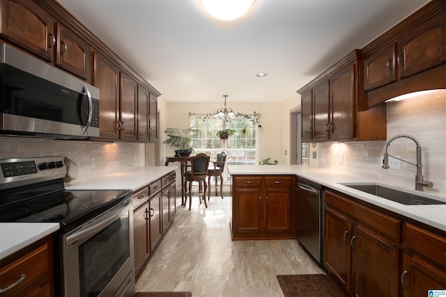 kitchen with appliances with stainless steel finishes, backsplash, sink, pendant lighting, and a notable chandelier