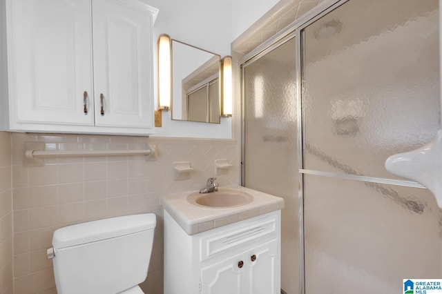 bathroom featuring vanity, toilet, a shower with shower door, and tile walls