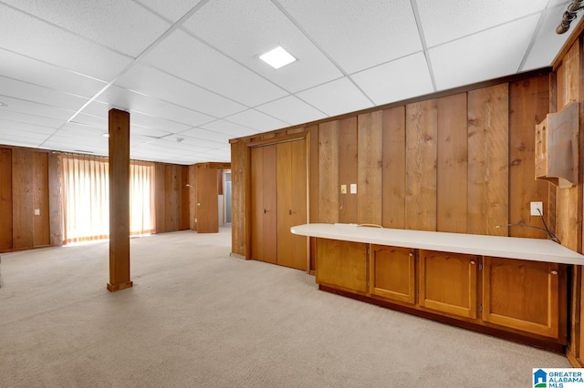 basement featuring light carpet, a paneled ceiling, and wood walls