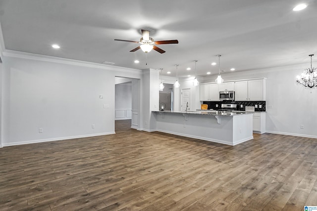 kitchen with a kitchen bar, appliances with stainless steel finishes, pendant lighting, hardwood / wood-style flooring, and white cabinetry