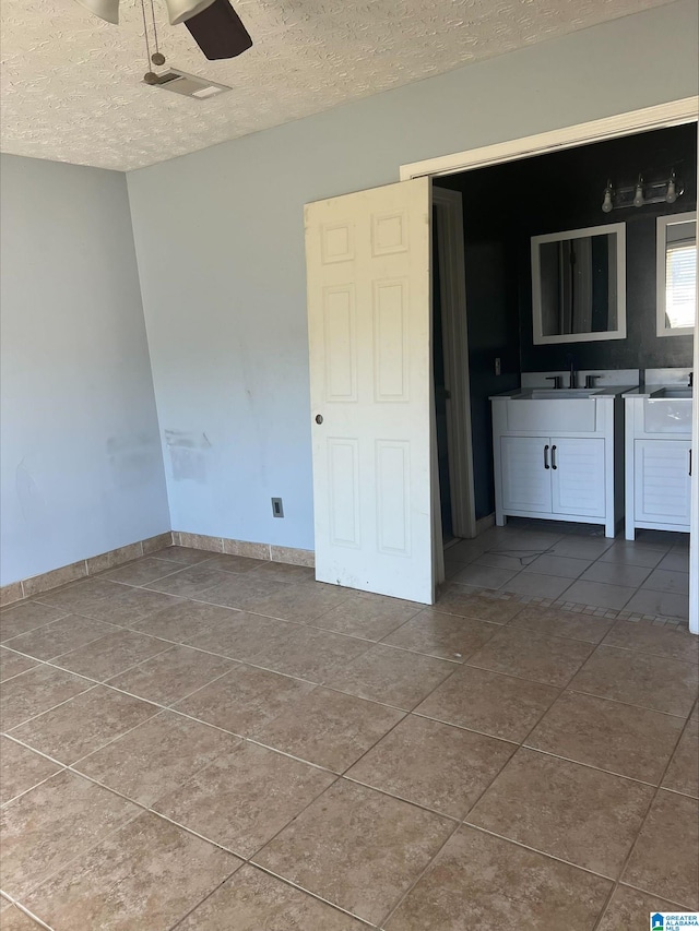 tiled empty room featuring ceiling fan, sink, and a textured ceiling