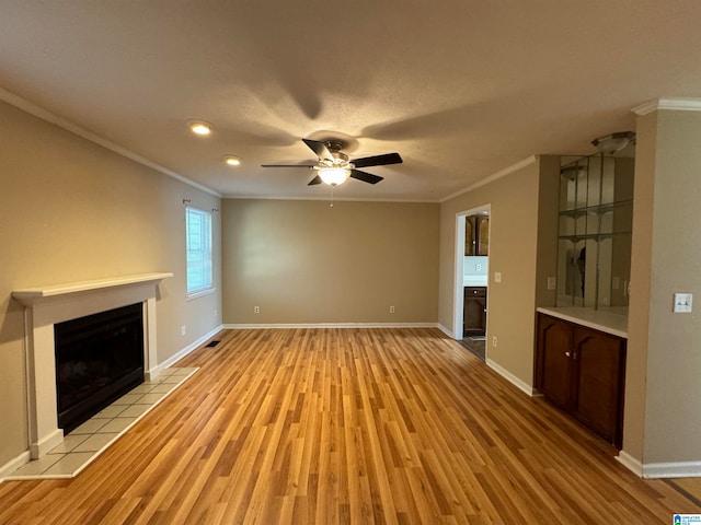 unfurnished living room with ceiling fan, light hardwood / wood-style floors, ornamental molding, and a tile fireplace