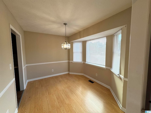 unfurnished dining area with a notable chandelier, wood-type flooring, and a textured ceiling