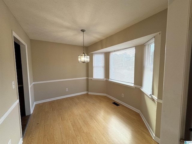 5807 Woodgate Cir, Anniston, AL 36207 - unfurnished room with light wood finished floors, healthy amount of natural light, a chandelier, baseboards, and a textured ceiling