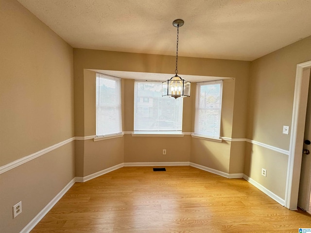 unfurnished dining area with a textured ceiling, light hardwood / wood-style flooring, and a notable chandelier