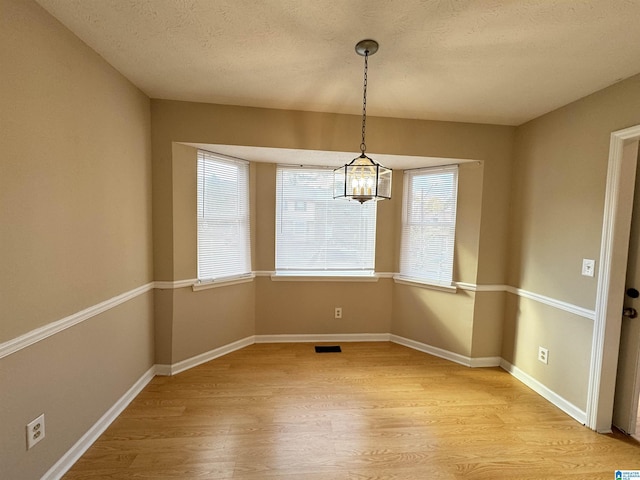 5807 Woodgate Cir, Anniston, AL 36207 - unfurnished dining area featuring light wood-type flooring, a chandelier, a textured ceiling, and baseboards