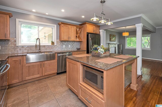 kitchen with appliances with stainless steel finishes, ornamental molding, sink, wood-type flooring, and a kitchen island