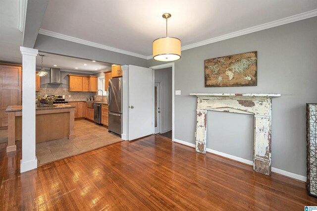 kitchen with light hardwood / wood-style flooring, wall chimney exhaust hood, ornamental molding, and appliances with stainless steel finishes