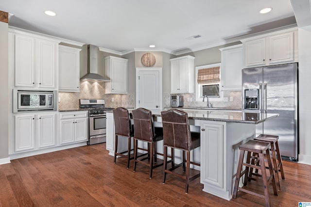 kitchen with appliances with stainless steel finishes, a breakfast bar, wall chimney range hood, a center island, and white cabinetry