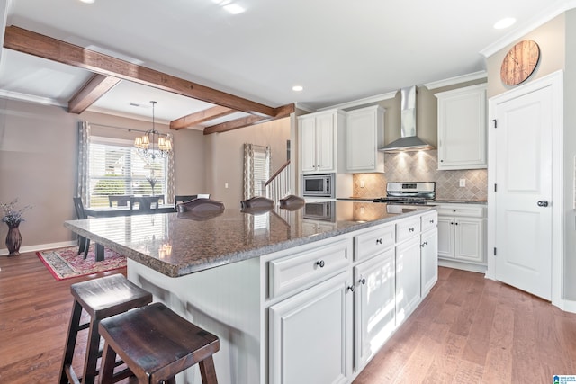 kitchen with beamed ceiling, wall chimney exhaust hood, a kitchen island, and light hardwood / wood-style flooring