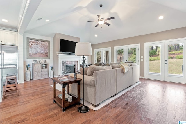 living room featuring lofted ceiling, french doors, ceiling fan, a fireplace, and light hardwood / wood-style floors