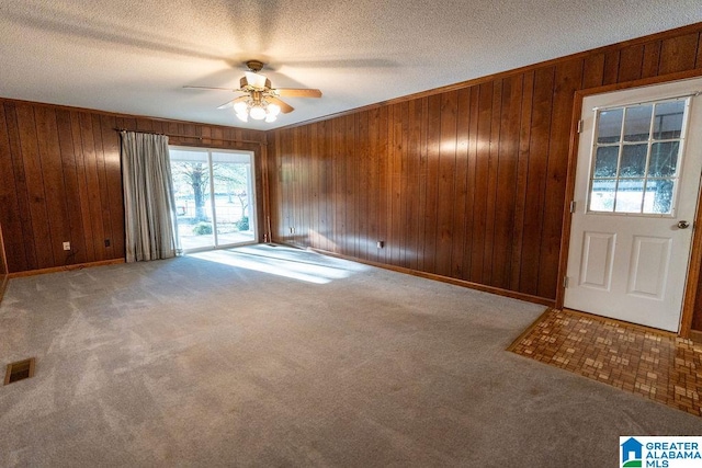 foyer entrance with a textured ceiling, ceiling fan, carpet floors, and wood walls