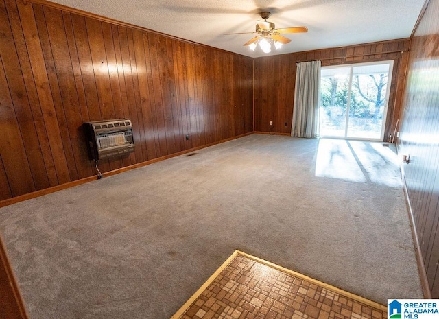 empty room with wood walls, ceiling fan, a textured ceiling, carpet floors, and heating unit