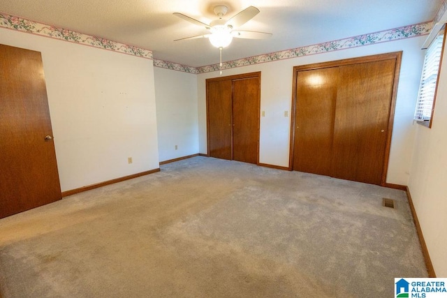 unfurnished bedroom featuring multiple closets, ceiling fan, and light carpet