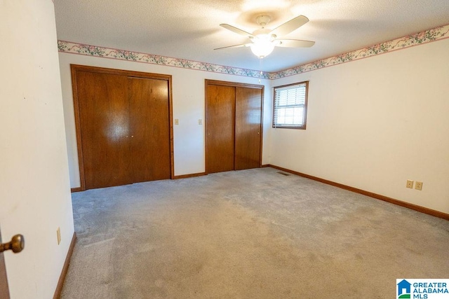 unfurnished bedroom featuring multiple closets, ceiling fan, light carpet, and a textured ceiling