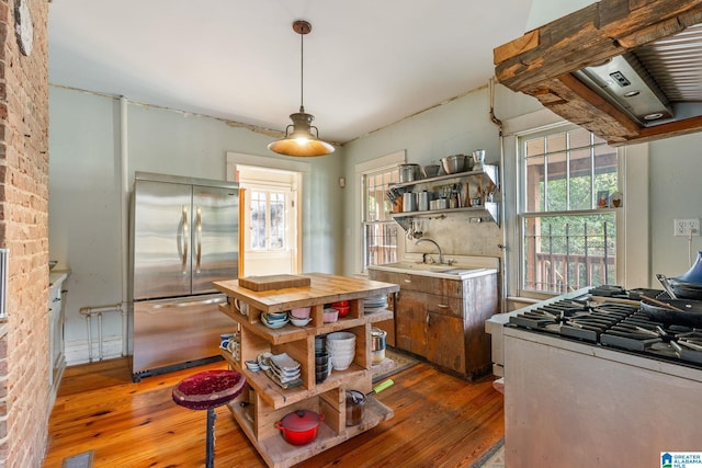 kitchen featuring dark wood-type flooring, sink, stainless steel fridge, brick wall, and range with gas cooktop