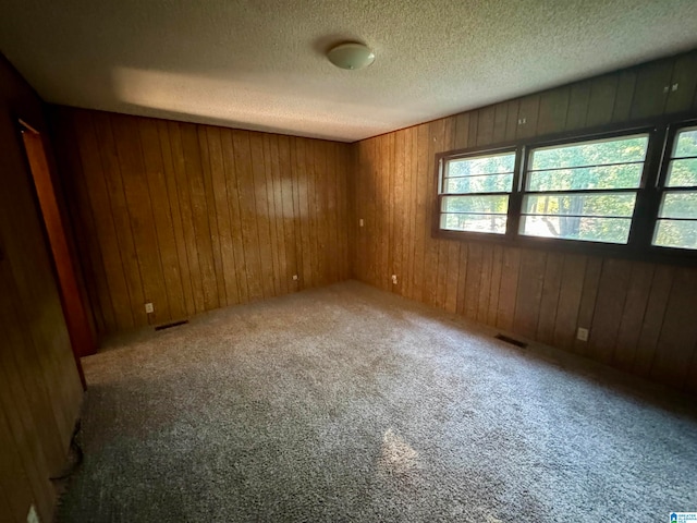 spare room featuring carpet floors, a textured ceiling, and wooden walls