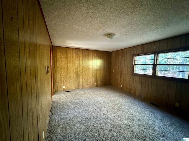 unfurnished room with a textured ceiling, carpet floors, and wood walls