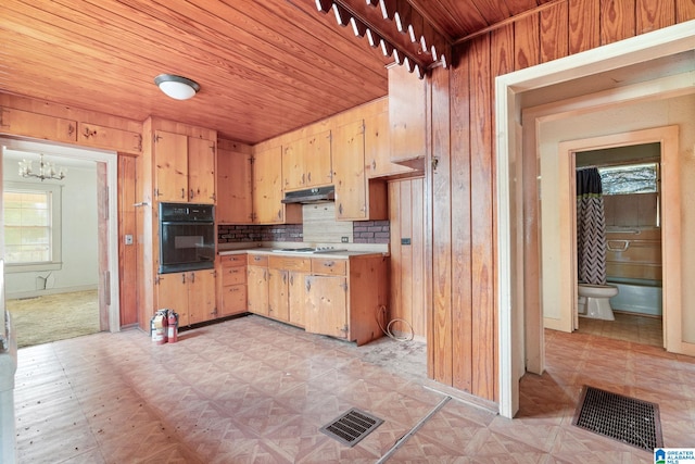 kitchen featuring gas cooktop, a notable chandelier, wood walls, black oven, and decorative backsplash